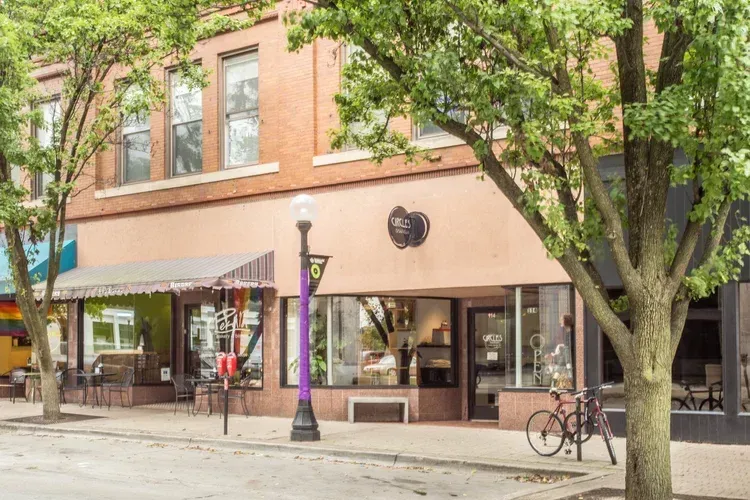 Street view of a brick storefront with trees, awning, windows, and a bicycle parked outside