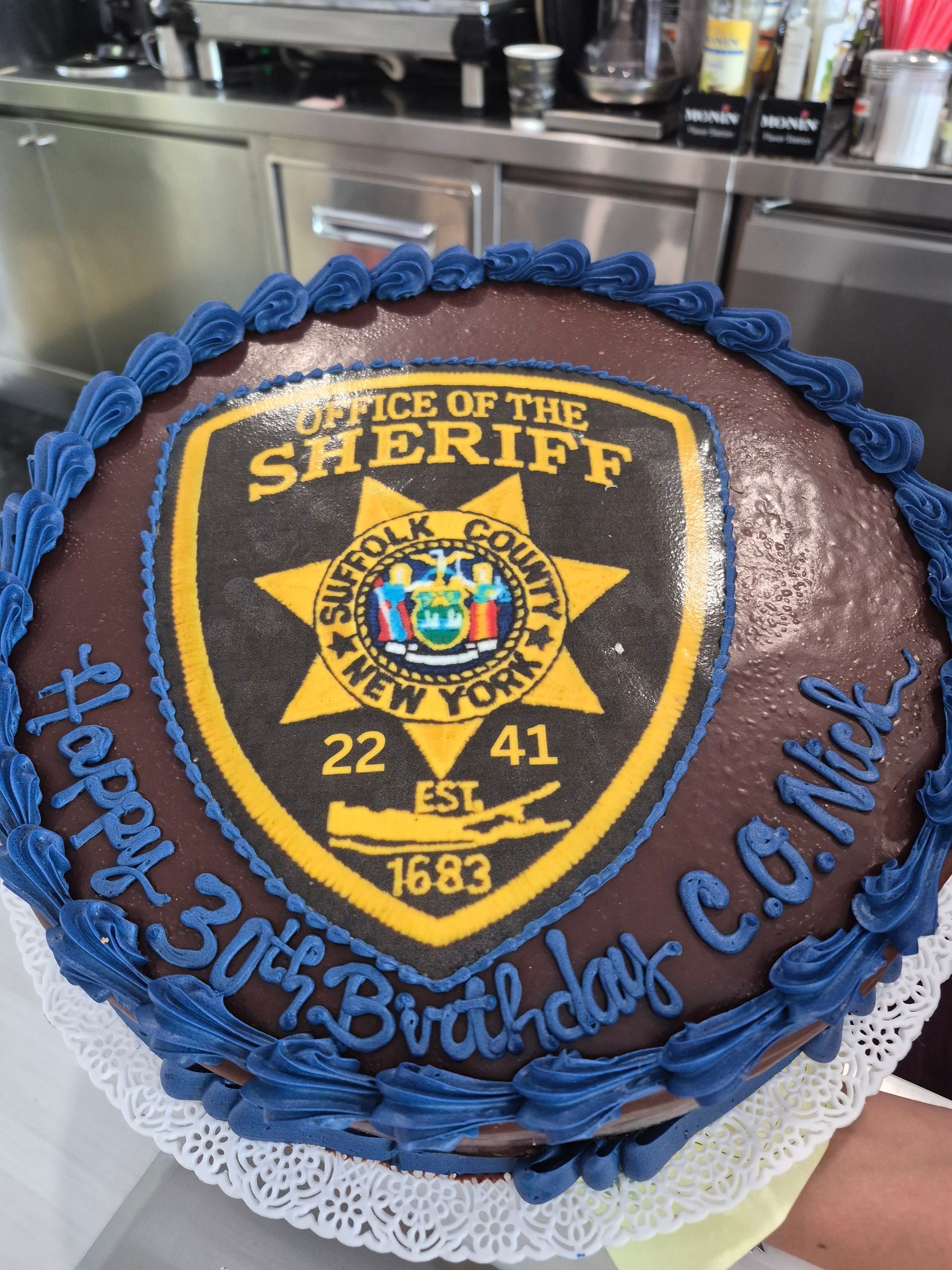 Sheriff badge birthday cake with blue rope border and “Happy 30th Birthday Cam” lettering