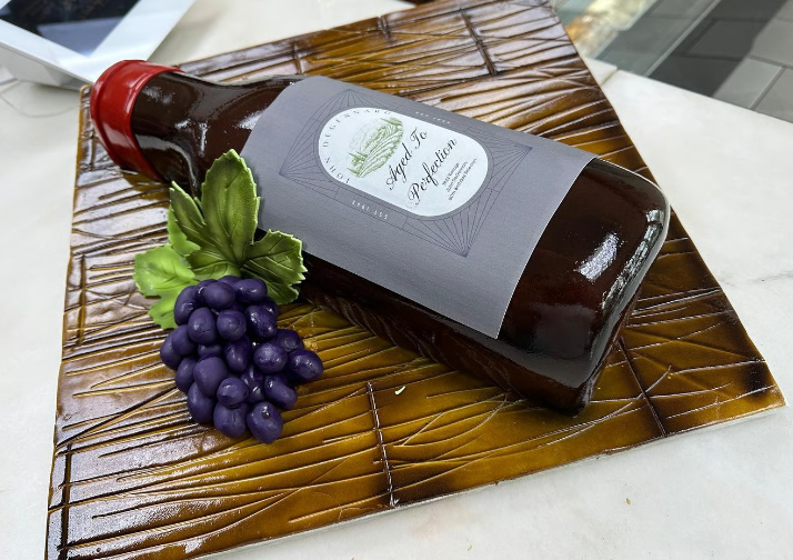 A cake that looks like a bottle of wine and a bunch of grapes.