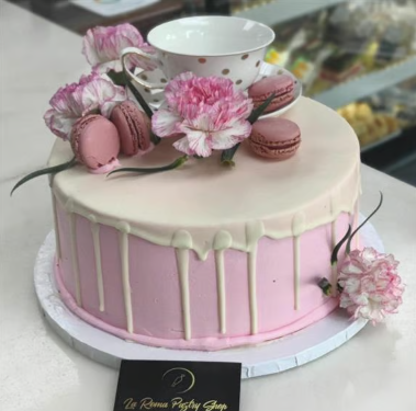 A pink and white cake with flowers and macarons on top