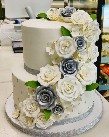 A wedding cake with white and silver roses on it