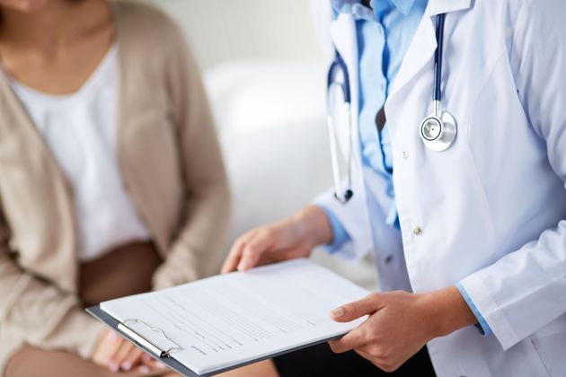 Doctor holding a clipboard while consulting with a seated patient in a clinic.