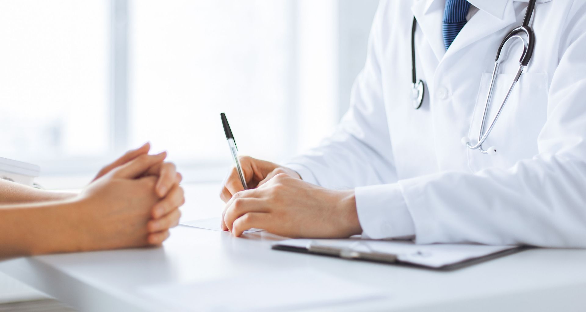 Doctor writing notes during a consultation with a patient at a desk.