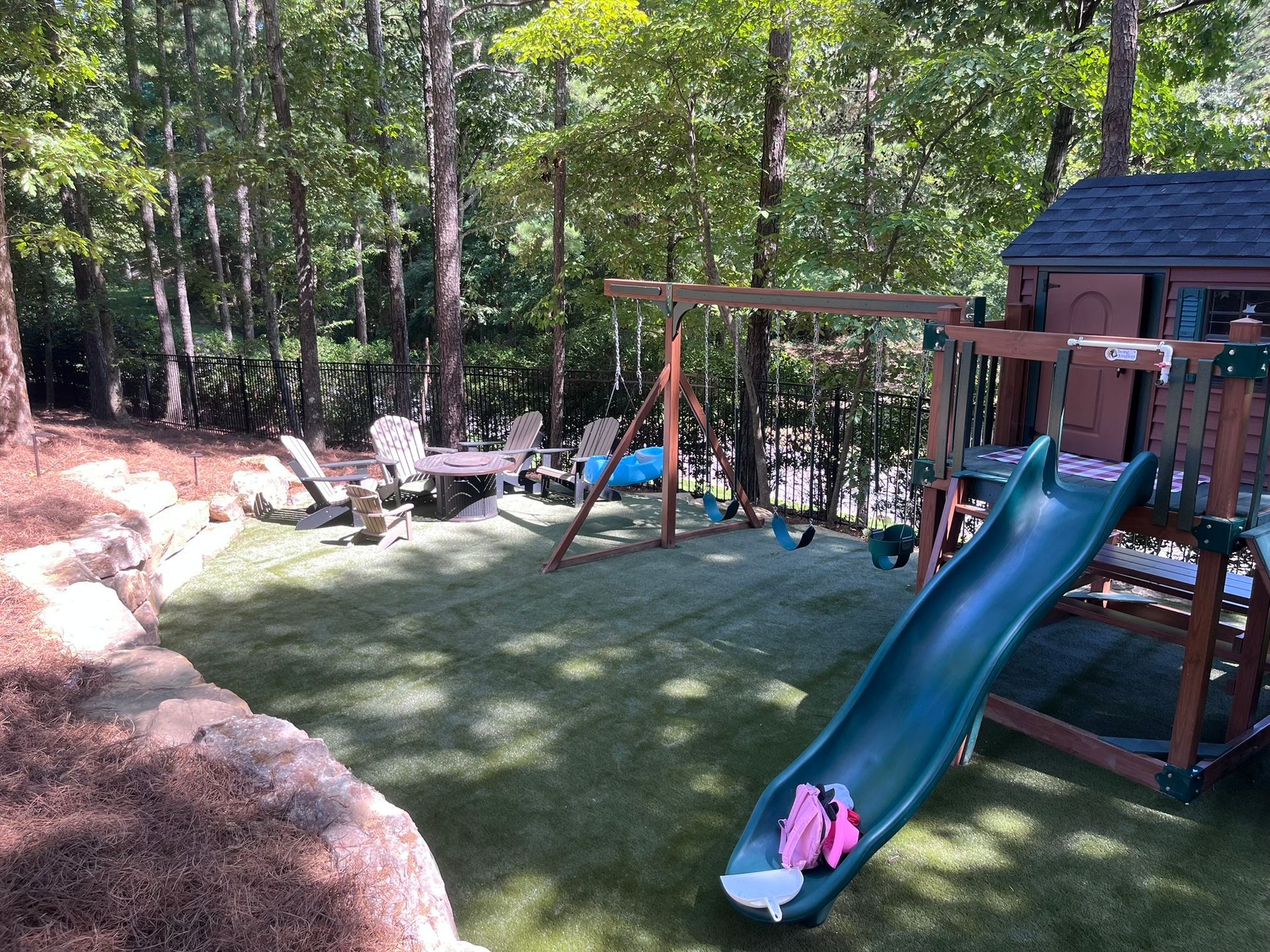 Playground with swing set, slide, and artificial turf in a wooded backyard setting.