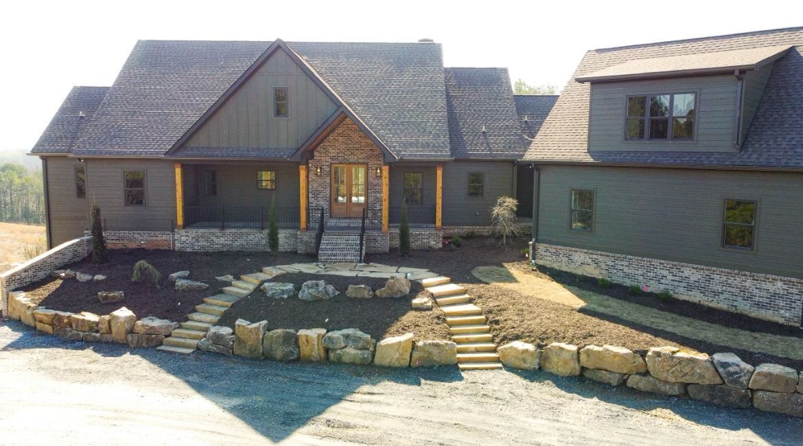 Modern house with stone facade and dark gray siding; stone steps lead to the front door.