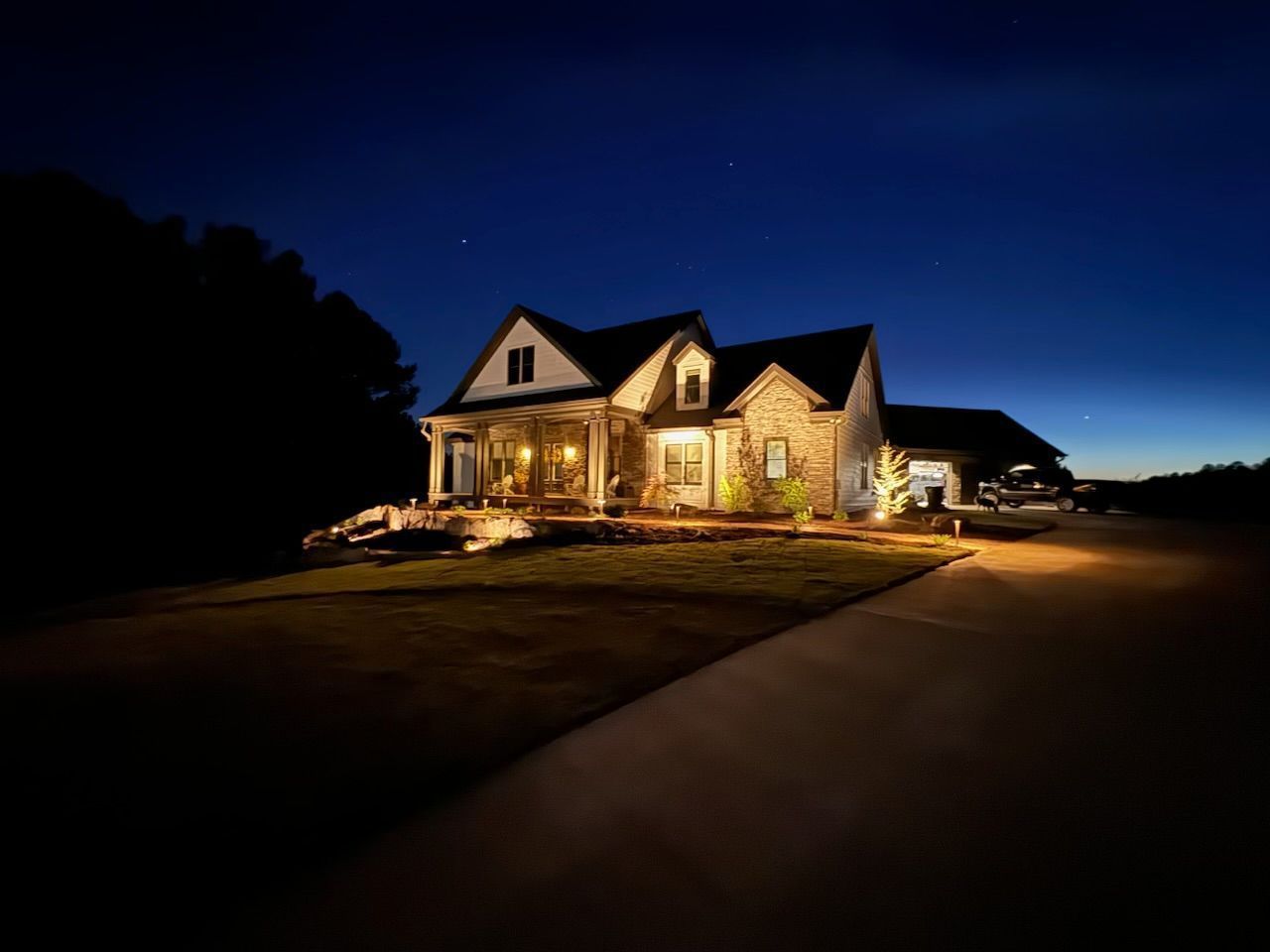 House illuminated at night with porch lights, driveway, and dark blue sky.