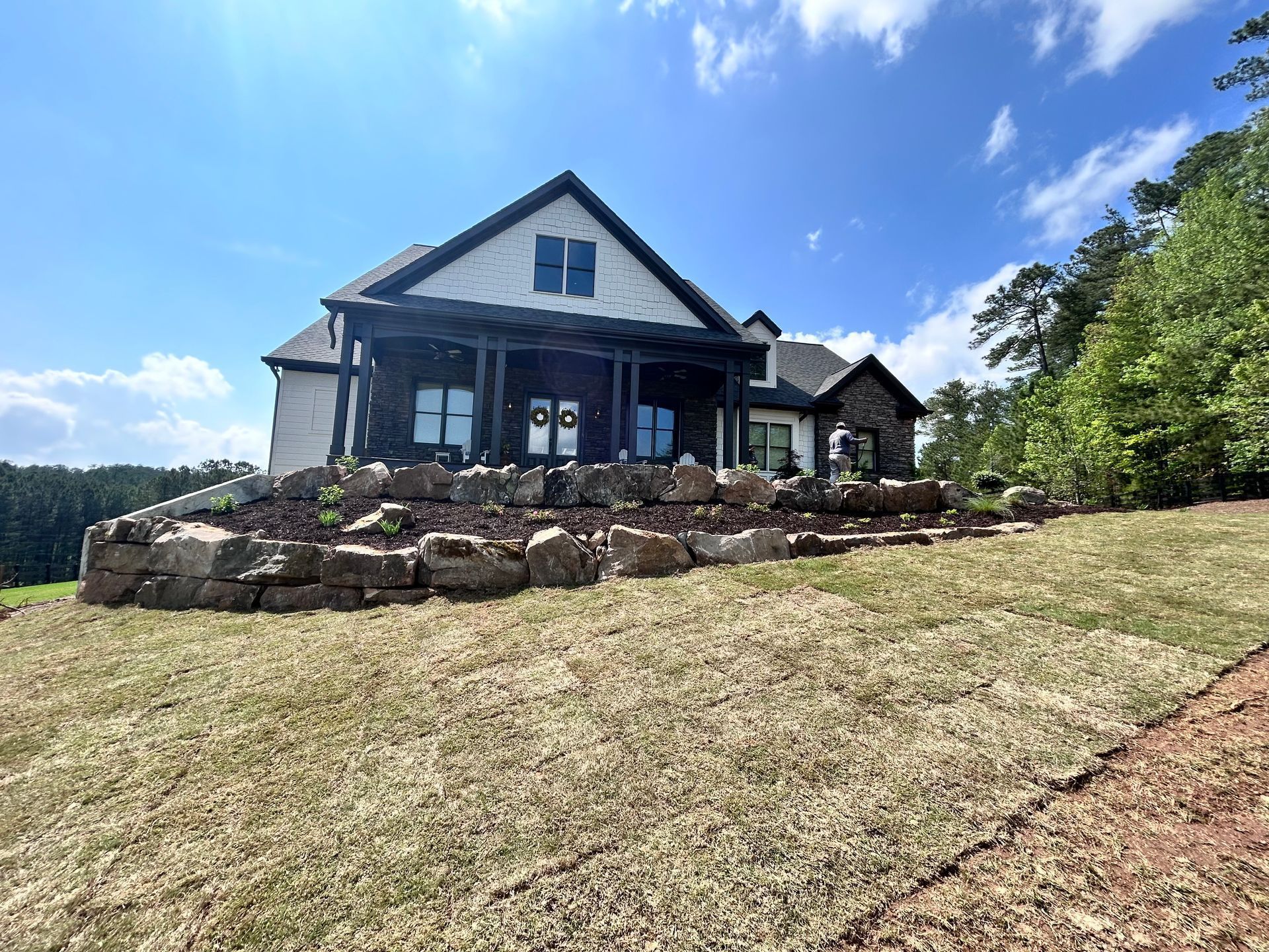 A large house with a stone retaining wall and a green lawn under a blue sky.