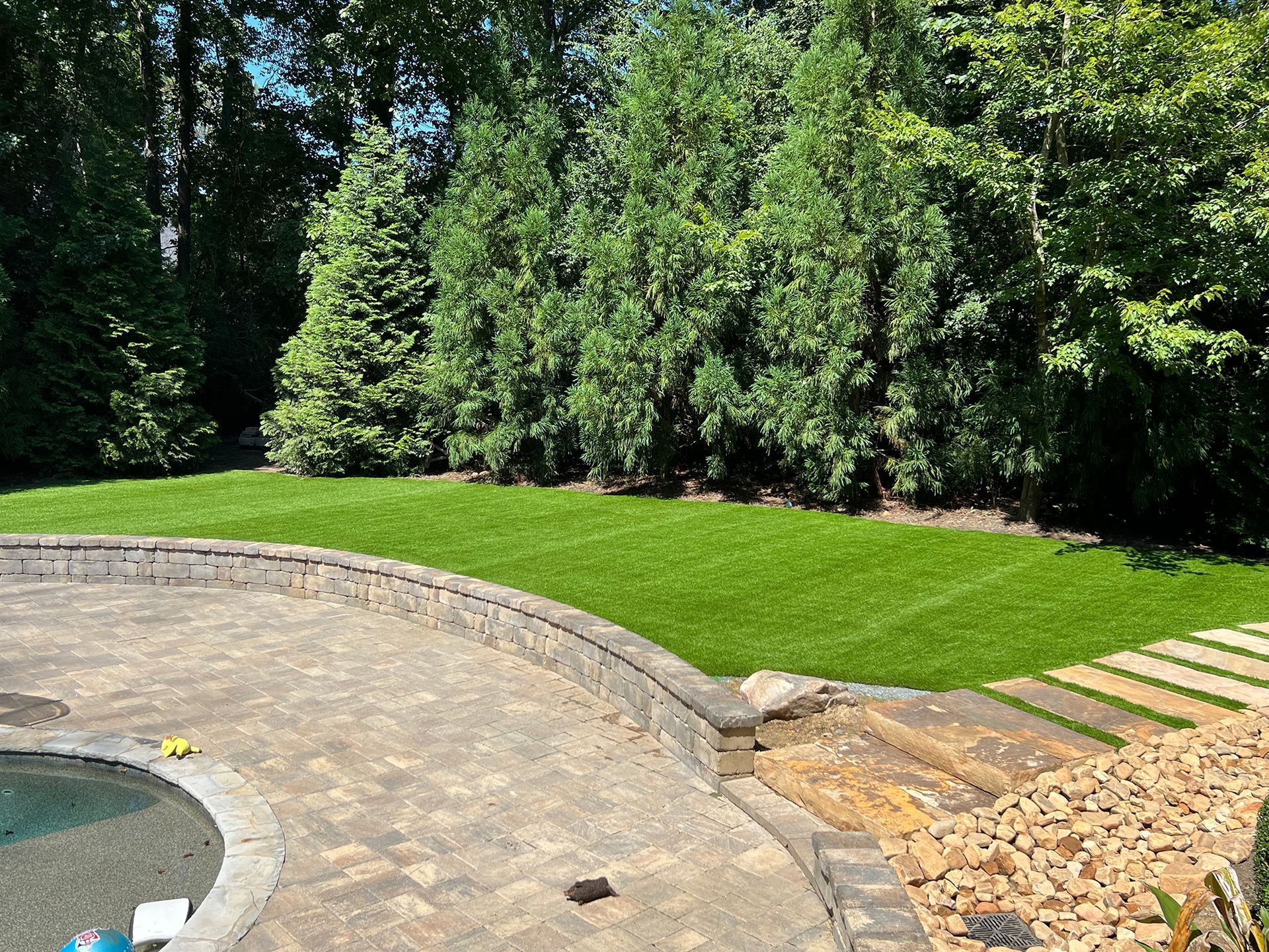 Backyard with a stone patio, lush green grass, and trees.