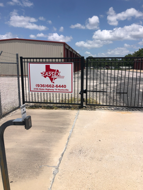 Metal gate entrance to Eastex Storage with a red and white sign displaying the company name, logo, and phone number.