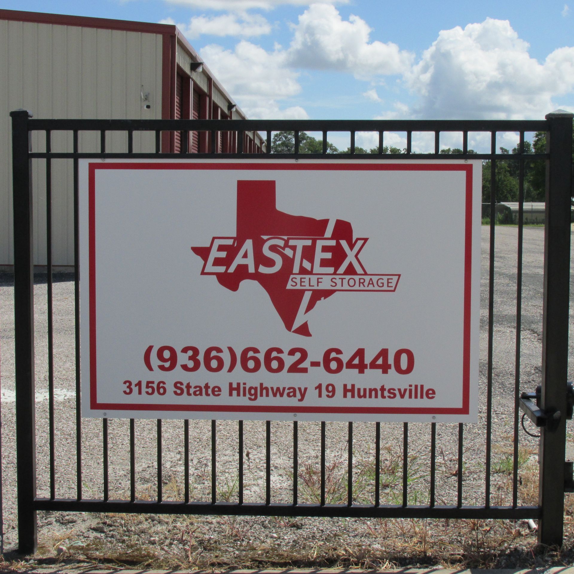 A red and white Eastex Self Storage sign on a black metal gate, listing phone number and address in Huntsville, Texas.