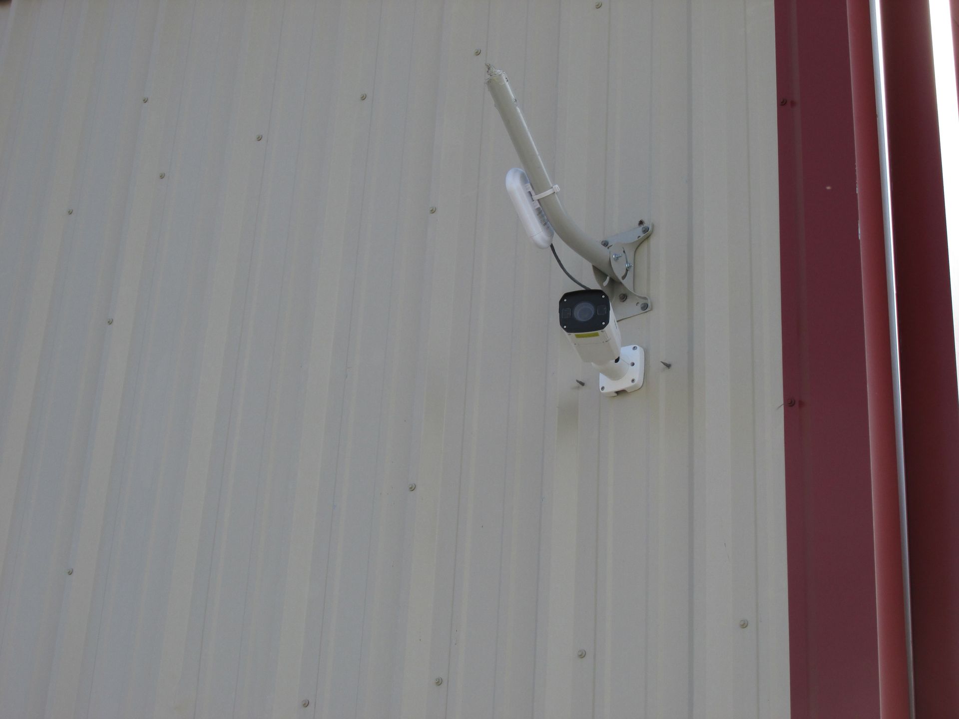 A white security camera mounted on a beige corrugated metal wall.