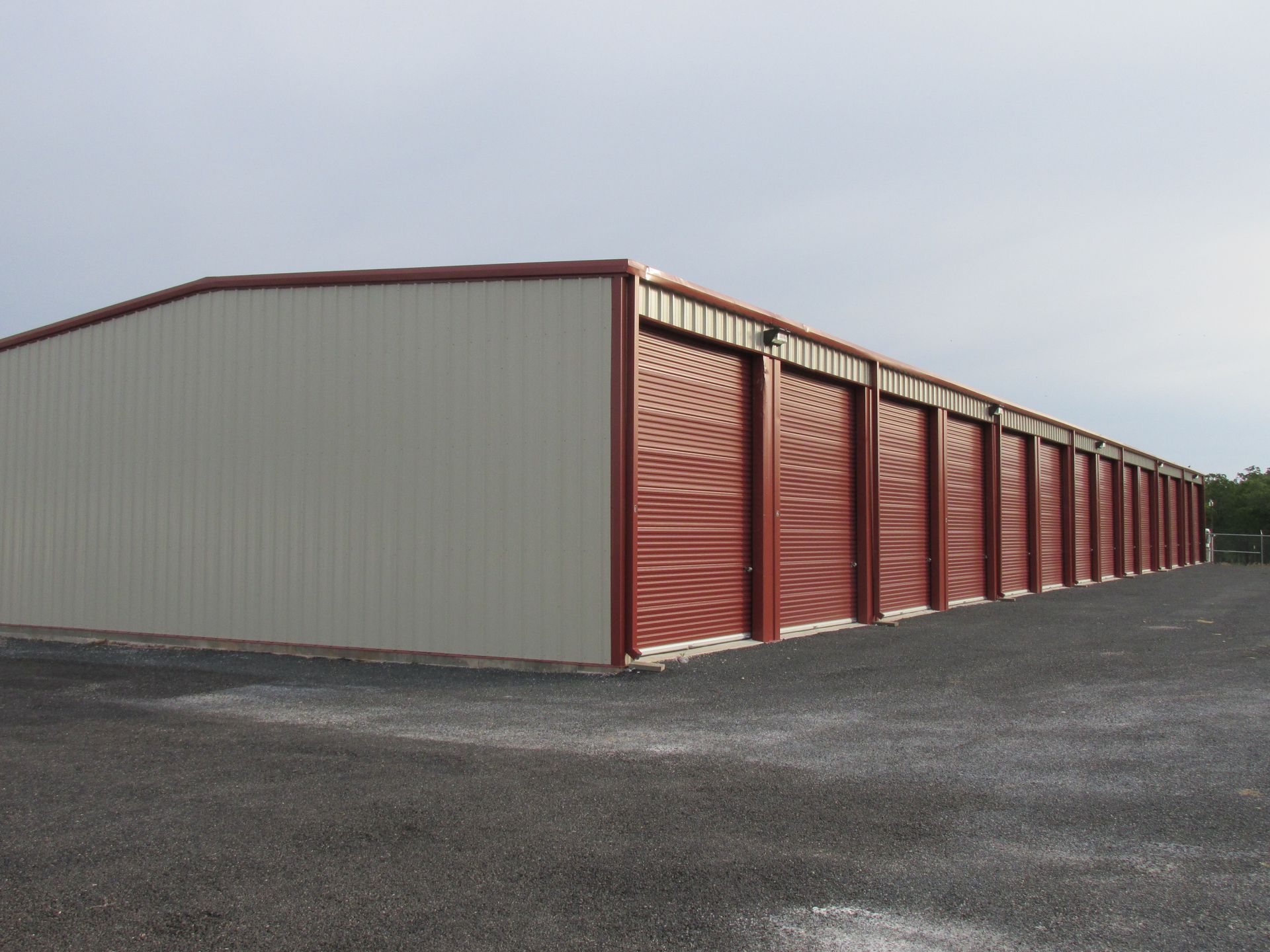 A row of grey industrial warehouse bays with yellow roll-up doors and rectangular windows under a blue, cloudy sky.
