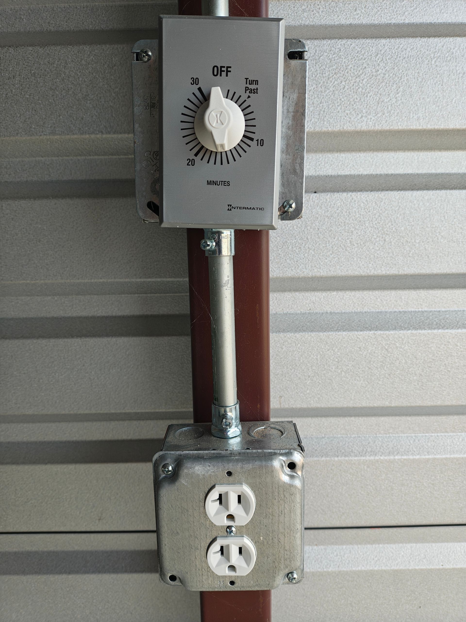 Wall switch and outlet mounted on a metal conduit against a corrugated wall.