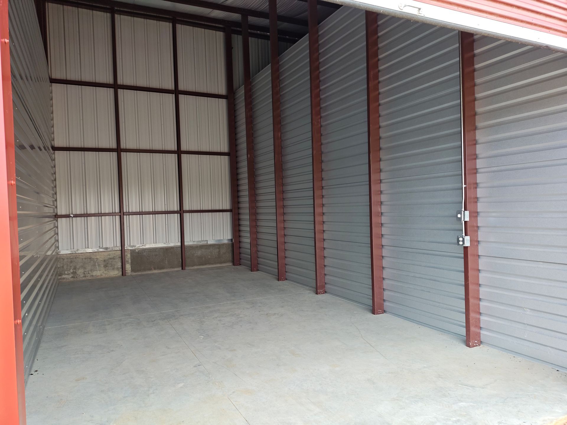 Empty corrugated metal storage unit with gray walls and concrete floor.