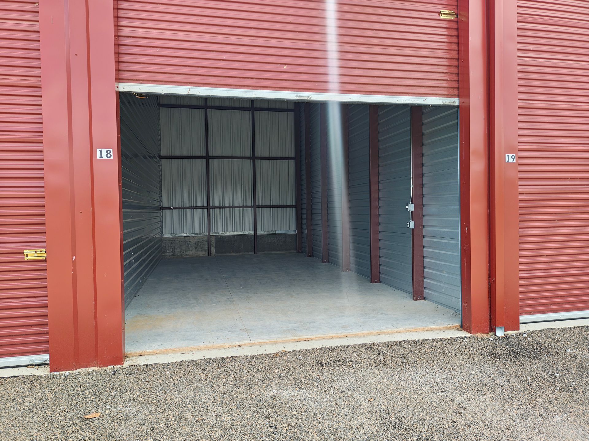 Open red garage storage unit with metal roll-up door and empty concrete floor.