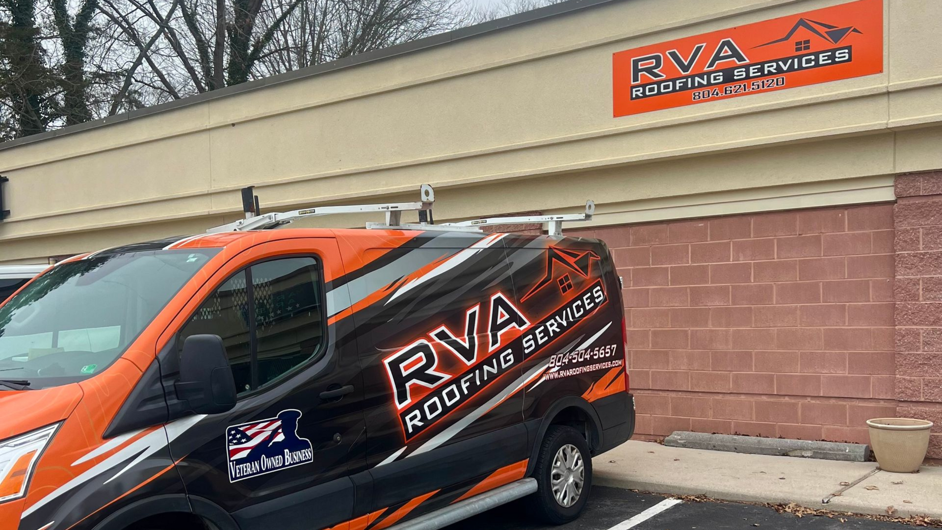 Black and orange RVA Roofing Services van parked outside a building.