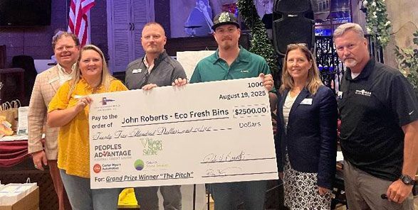 Group of people holding a large check, likely a donation. Indoor setting with people smiling.