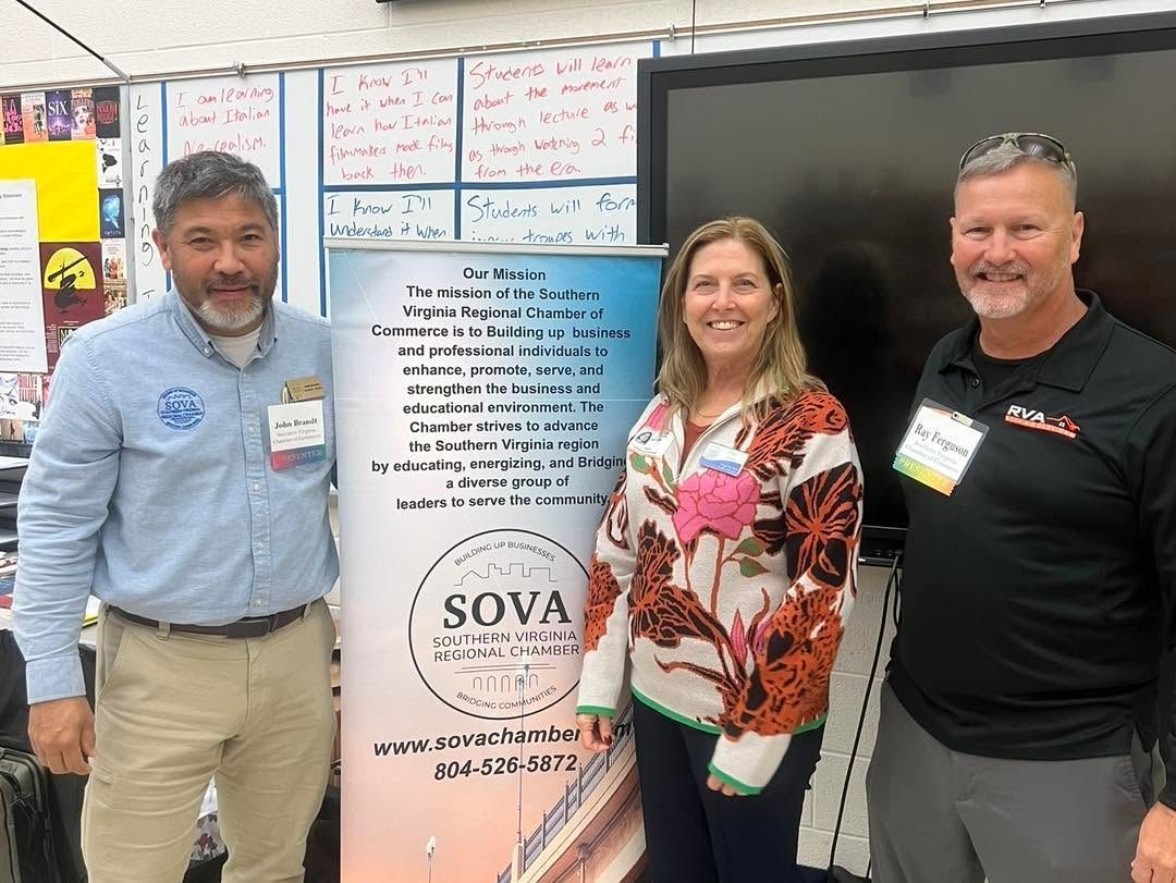 Three people posing beside a SOVA banner in a classroom with posters on the wall