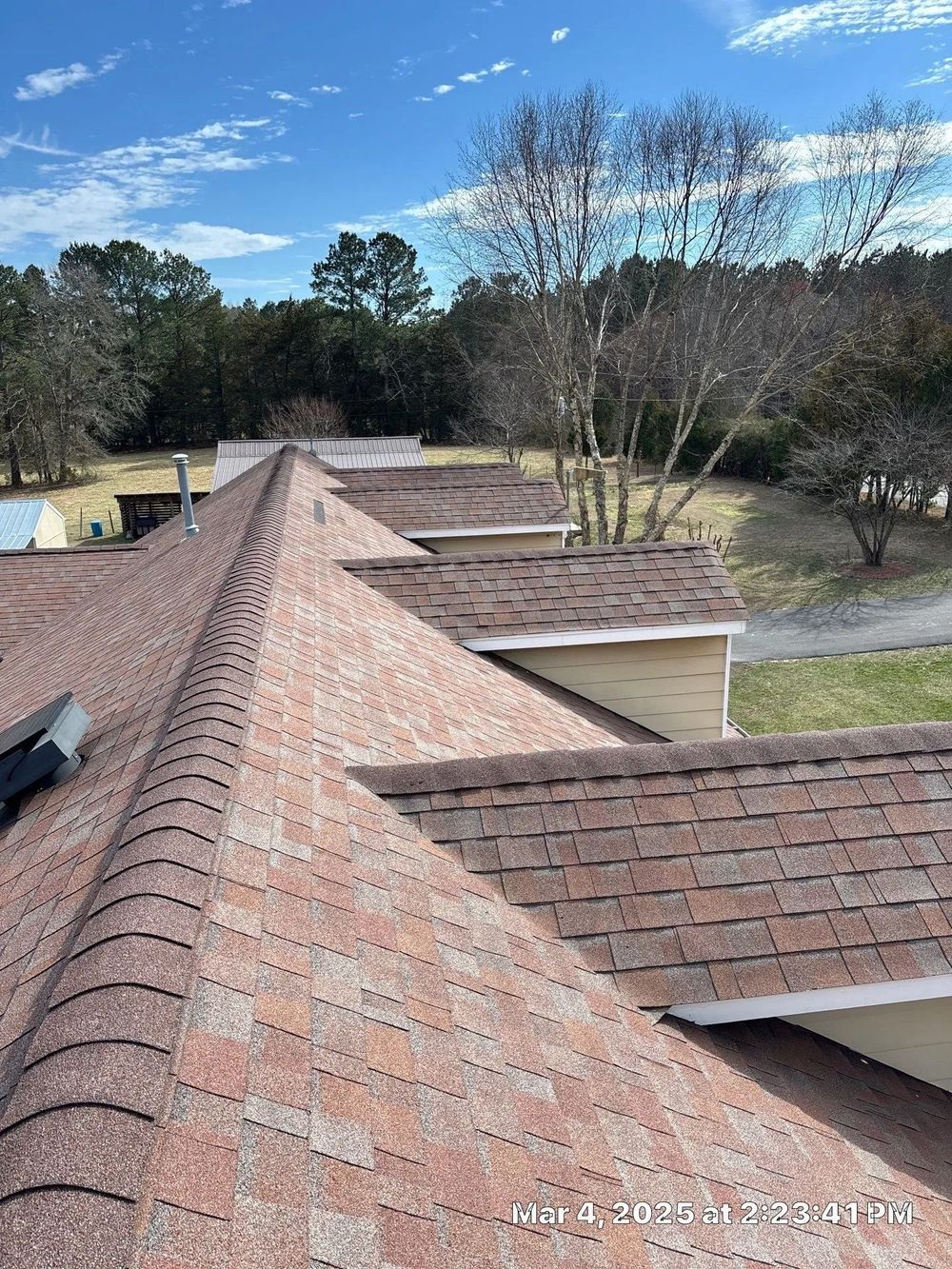Brown shingle roof on a building with trees and a blue sky in the background.