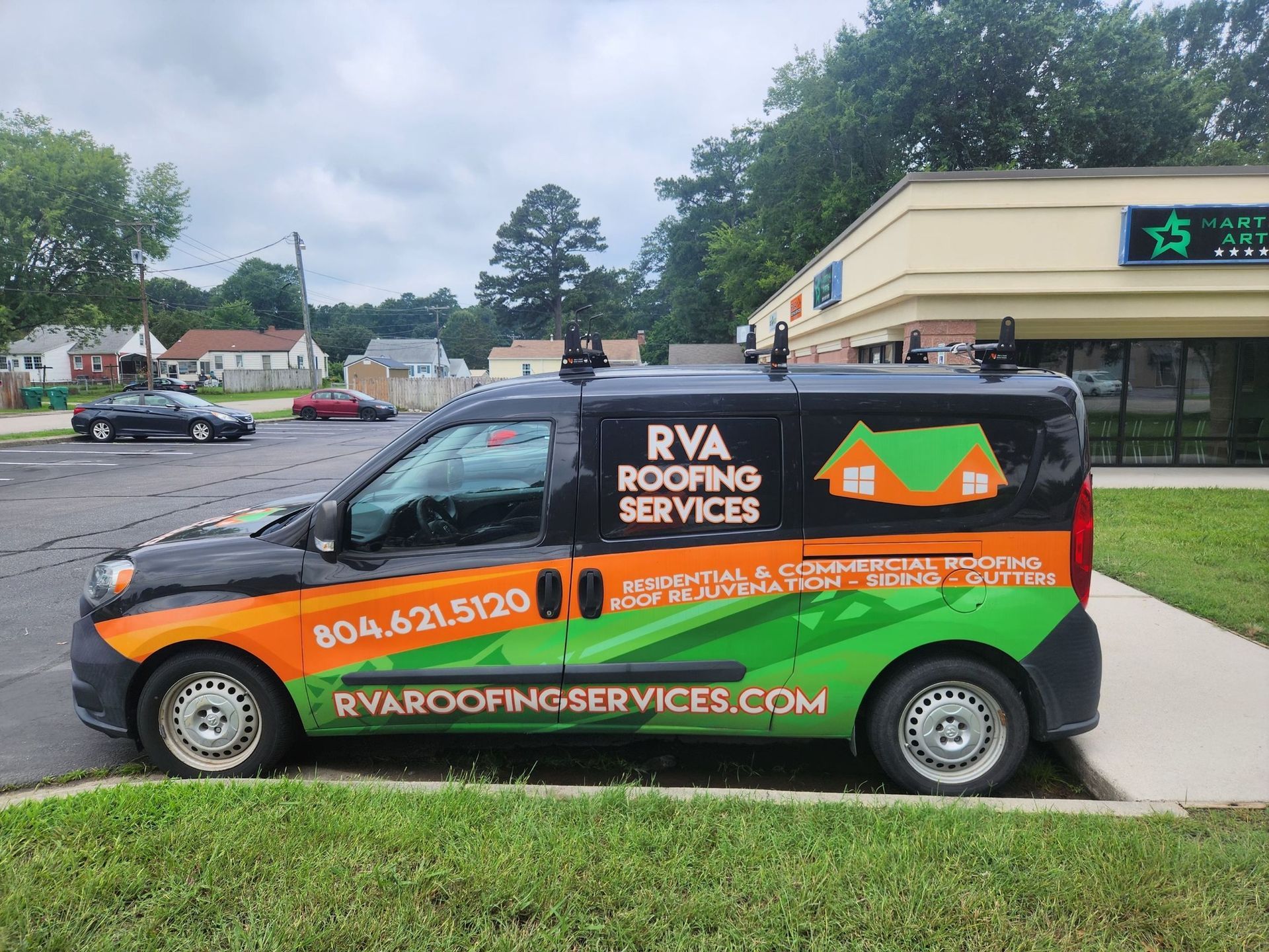 Black and orange RVA Roofing Services van parked outside a building.