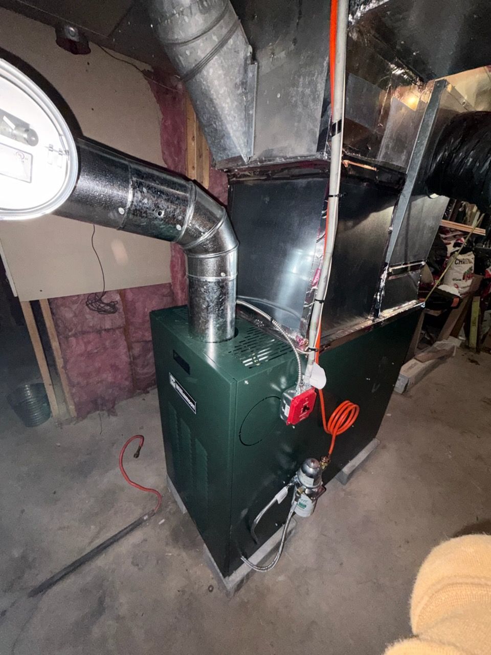 Green furnace with silver exhaust pipes, in a basement setting.