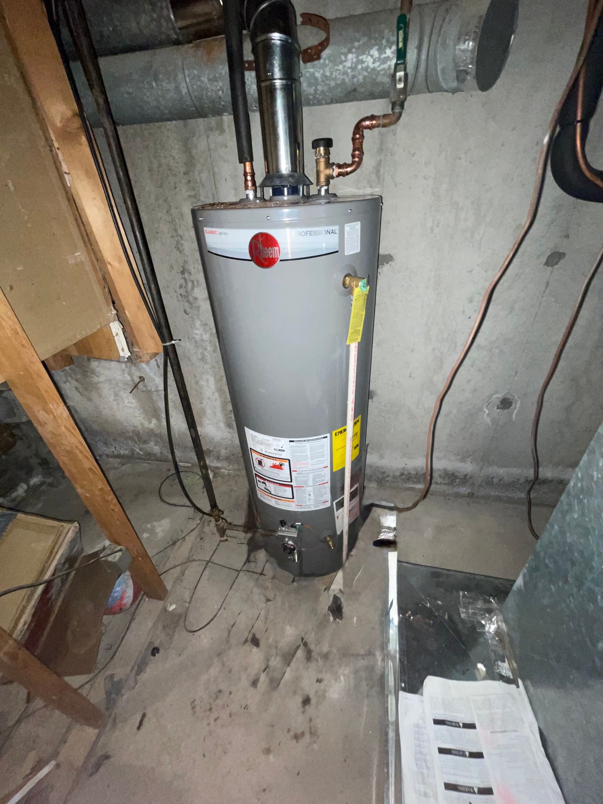 Gray water heater in a basement setting with various pipes and vents.