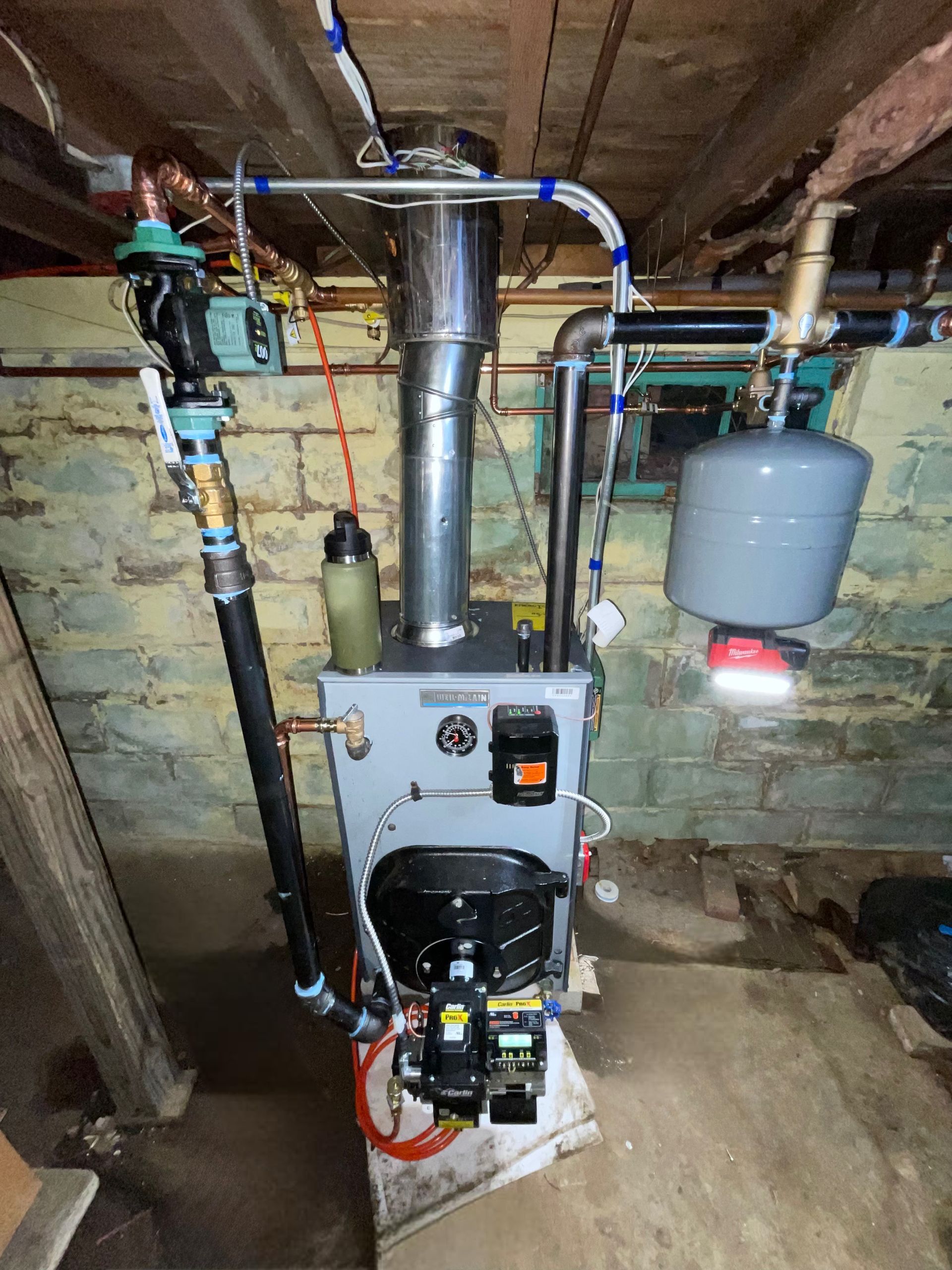 Oil furnace in basement with pipes, chimney, and expansion tank.