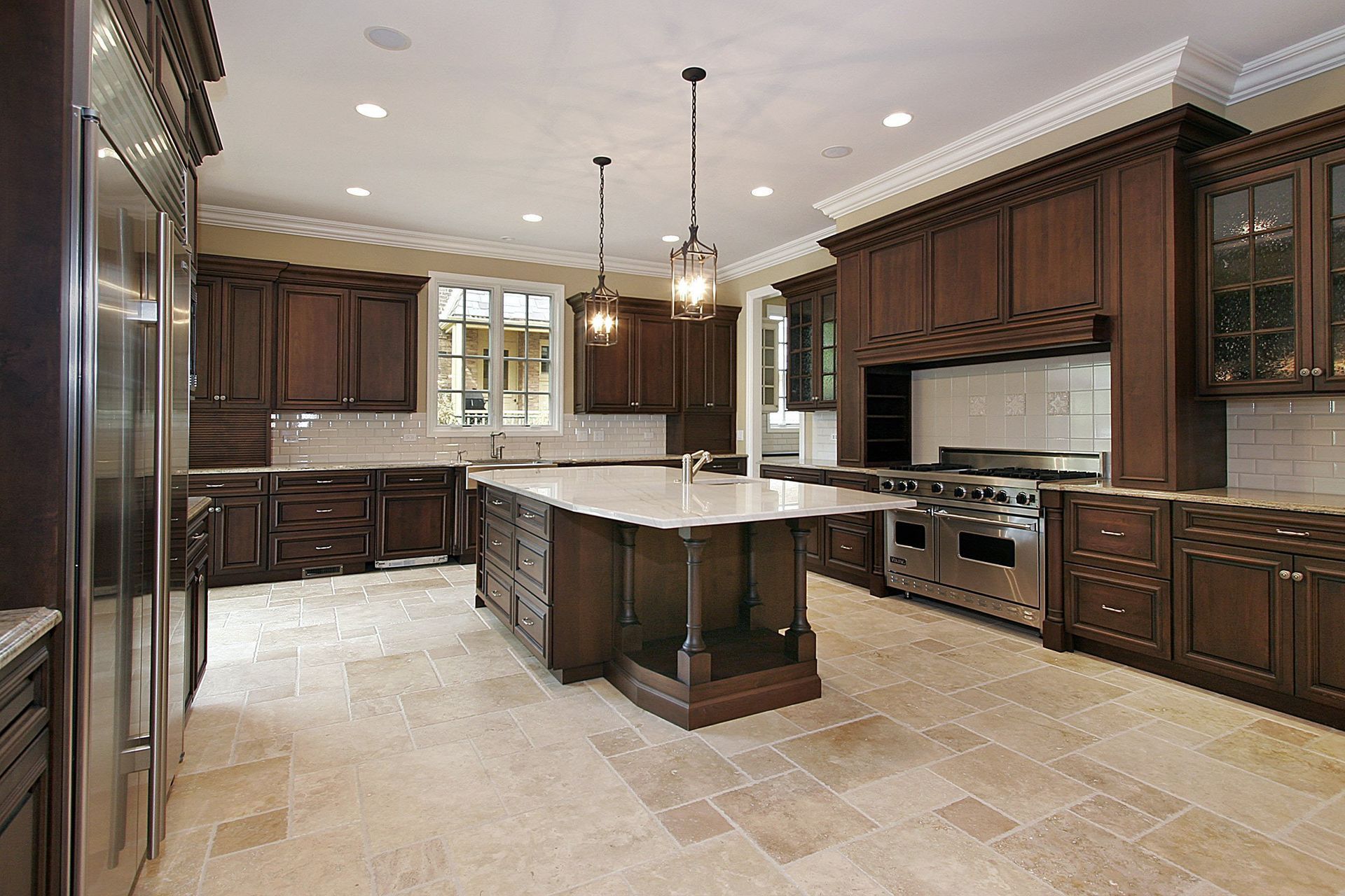 Elegant kitchen with dark wood cabinets, marble island, stainless steel appliances, and beige tile floor.