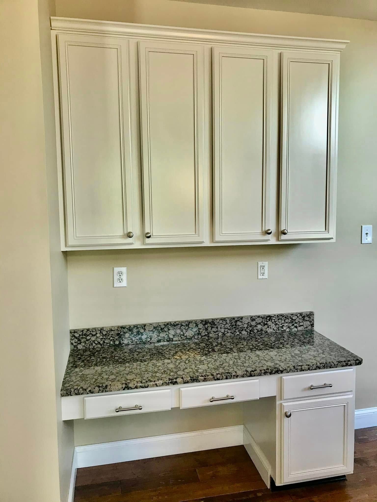 Built-in desk with granite countertop, white cabinets above and below, against a beige wall.