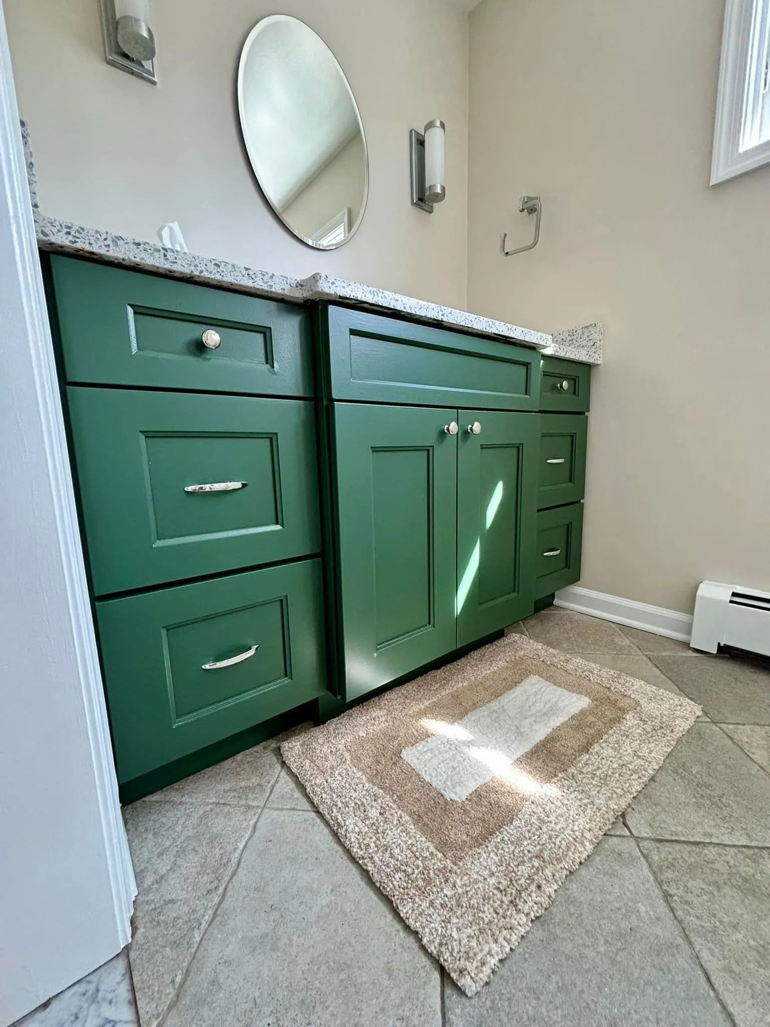 Green bathroom vanity with granite countertop, oval mirror, and beige rug.