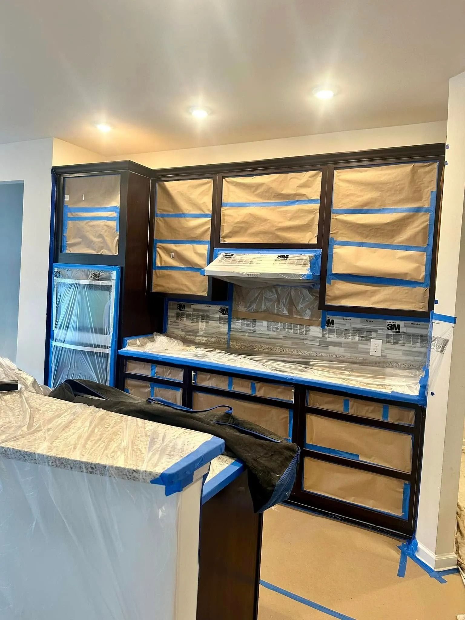 Kitchen cabinets taped and covered in preparation for painting. Brown cabinets with blue tape.