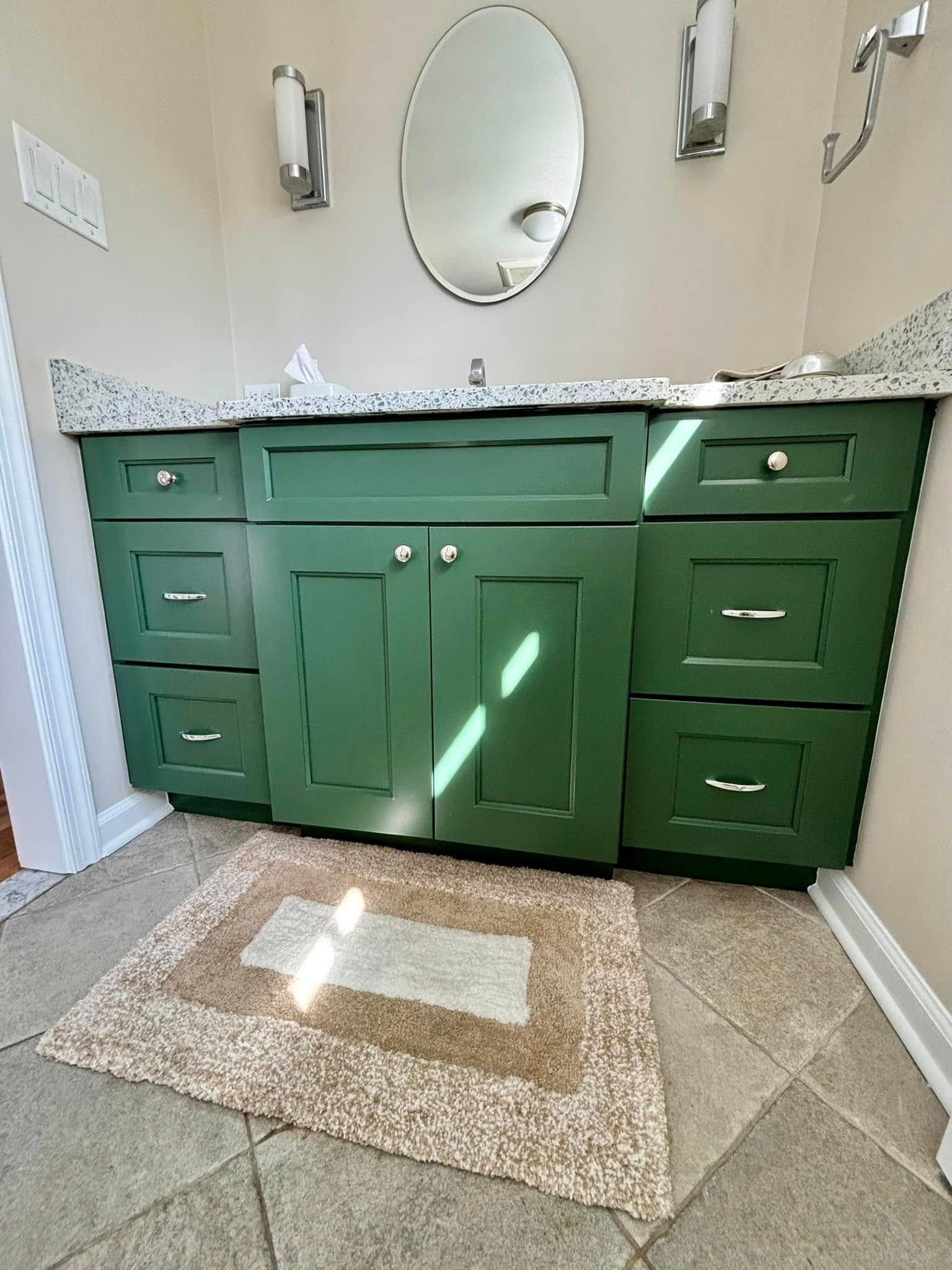 Green bathroom vanity with granite countertop, oval mirror, and rug.