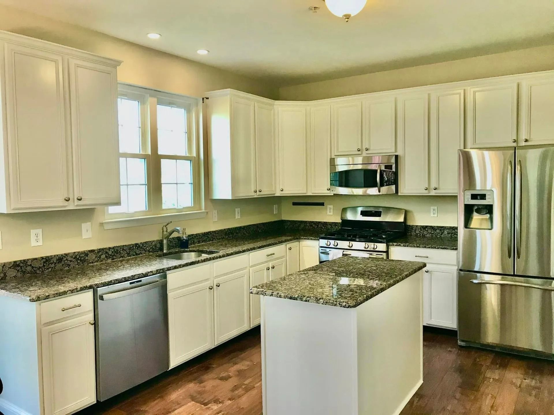 White kitchen with stainless steel appliances, granite countertops, and an island.