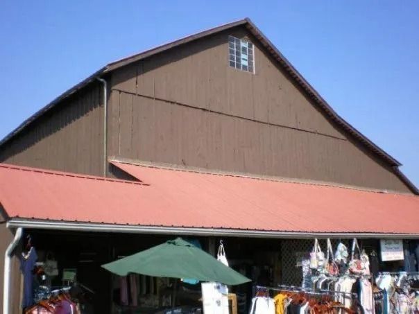 Brown barn-like building with a red roof, a small window, and a green umbrella. Merchandise is visible below.