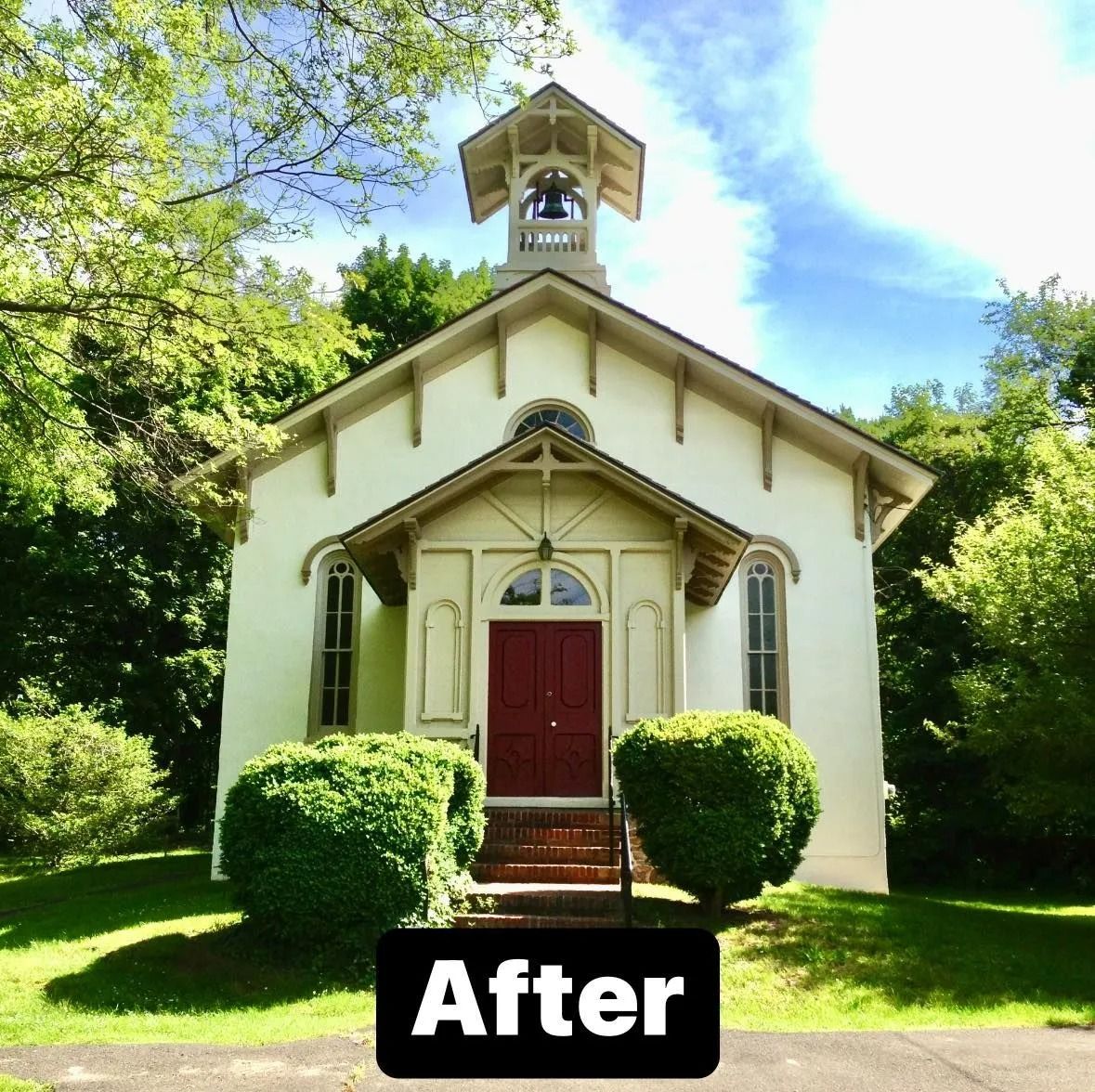 White church with red door and bell tower, surrounded by greenery under a blue sky.