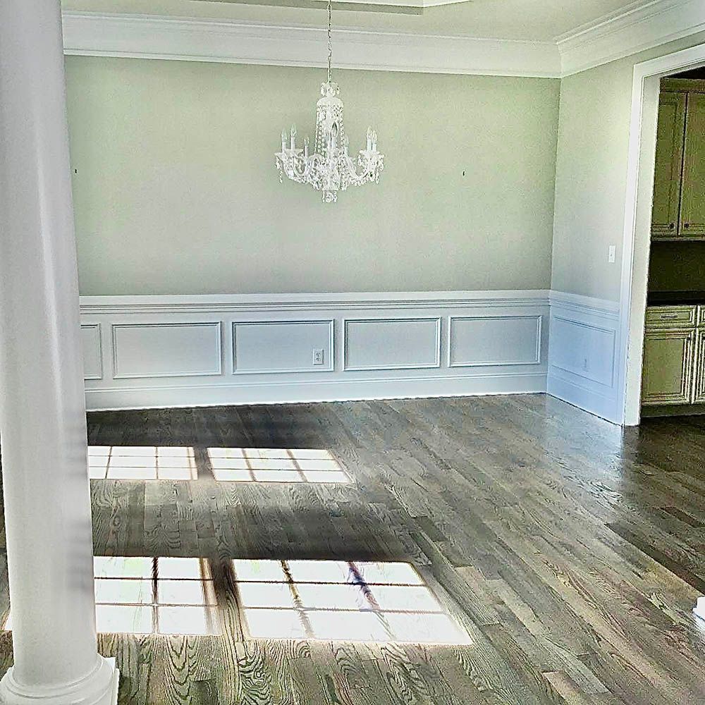 Empty dining room with chandelier, wooden floor, and paneling on the wall.