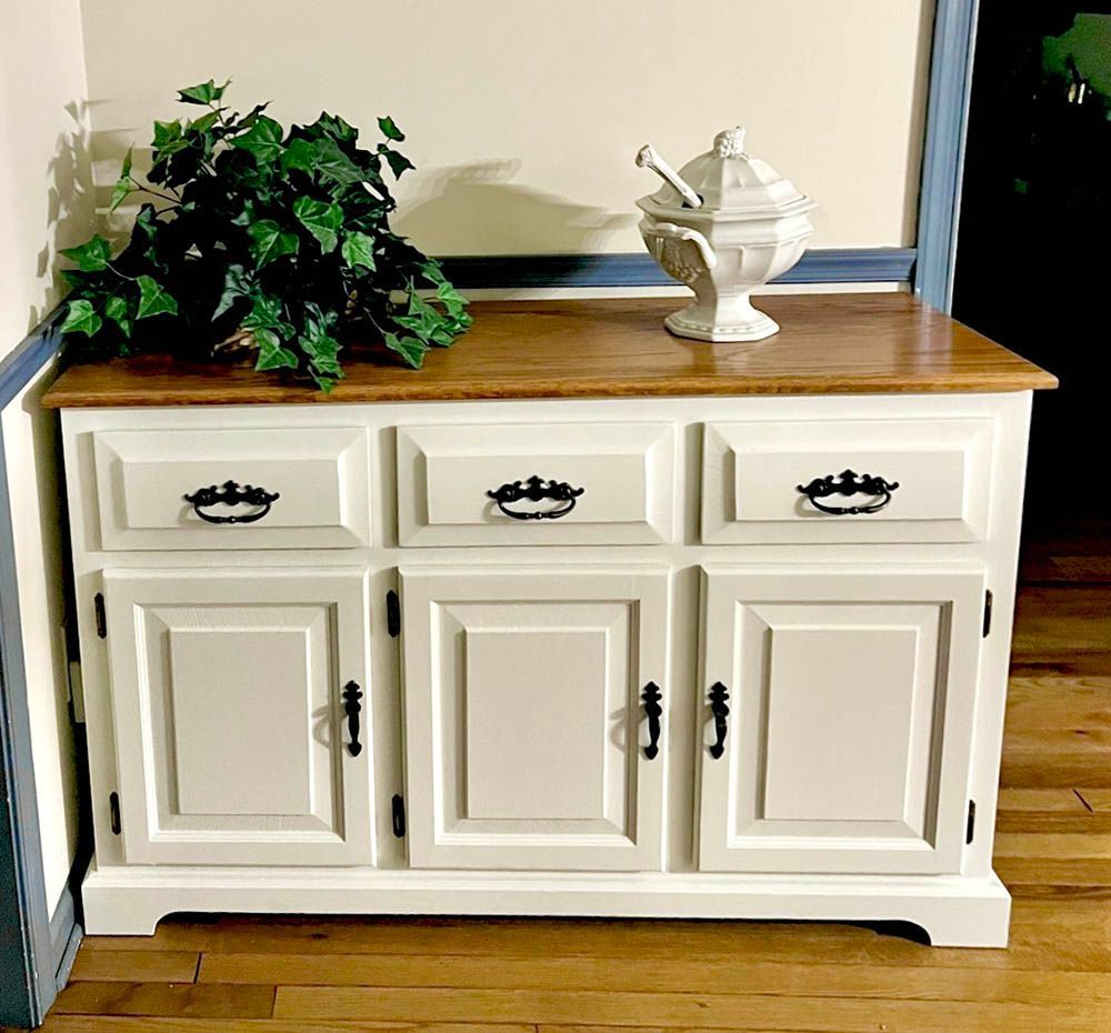 White buffet with wooden top. Plant and decorative dish on top.