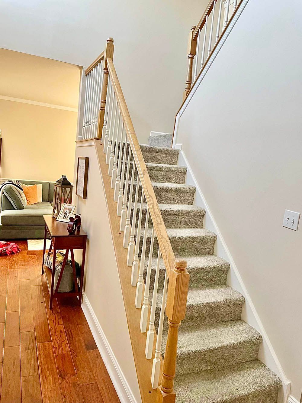 Staircase with carpeted steps and wooden railing. Light-colored walls and a view into a living room.