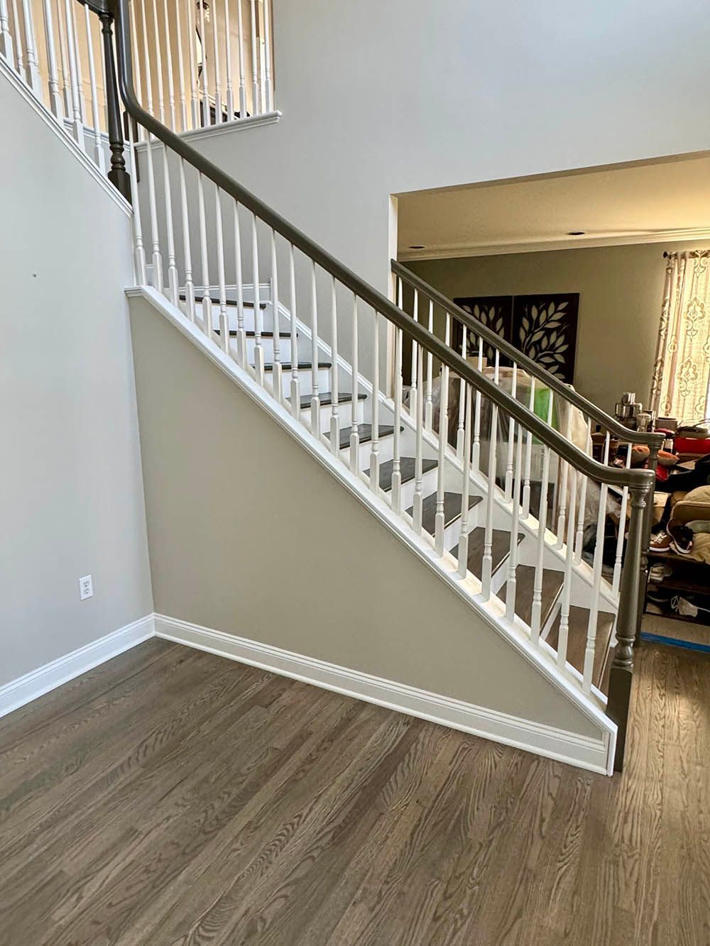 Staircase with white balusters, brown handrail, and tan wall against light wood floor.