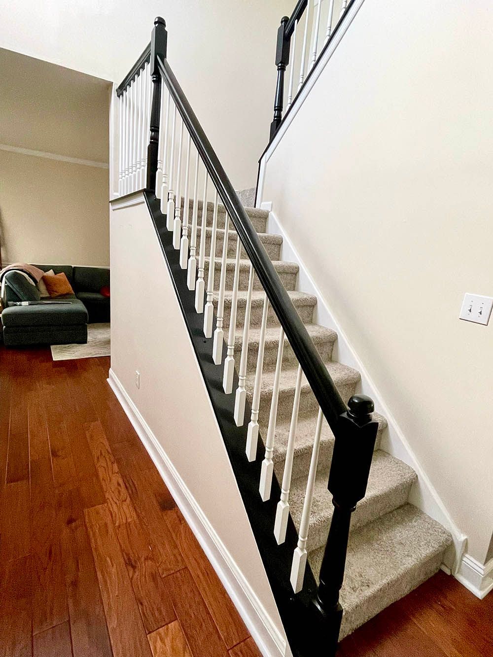 Staircase with black railing and white spindles, leading up to a second floor, hardwood floor in foreground.