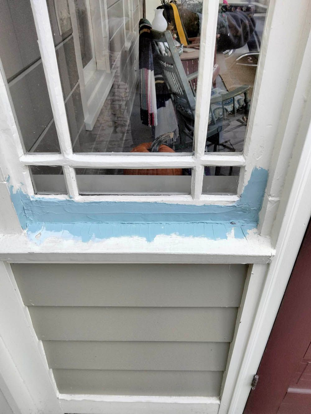 Window frame with painted blue trim above gray siding, next to a red door.