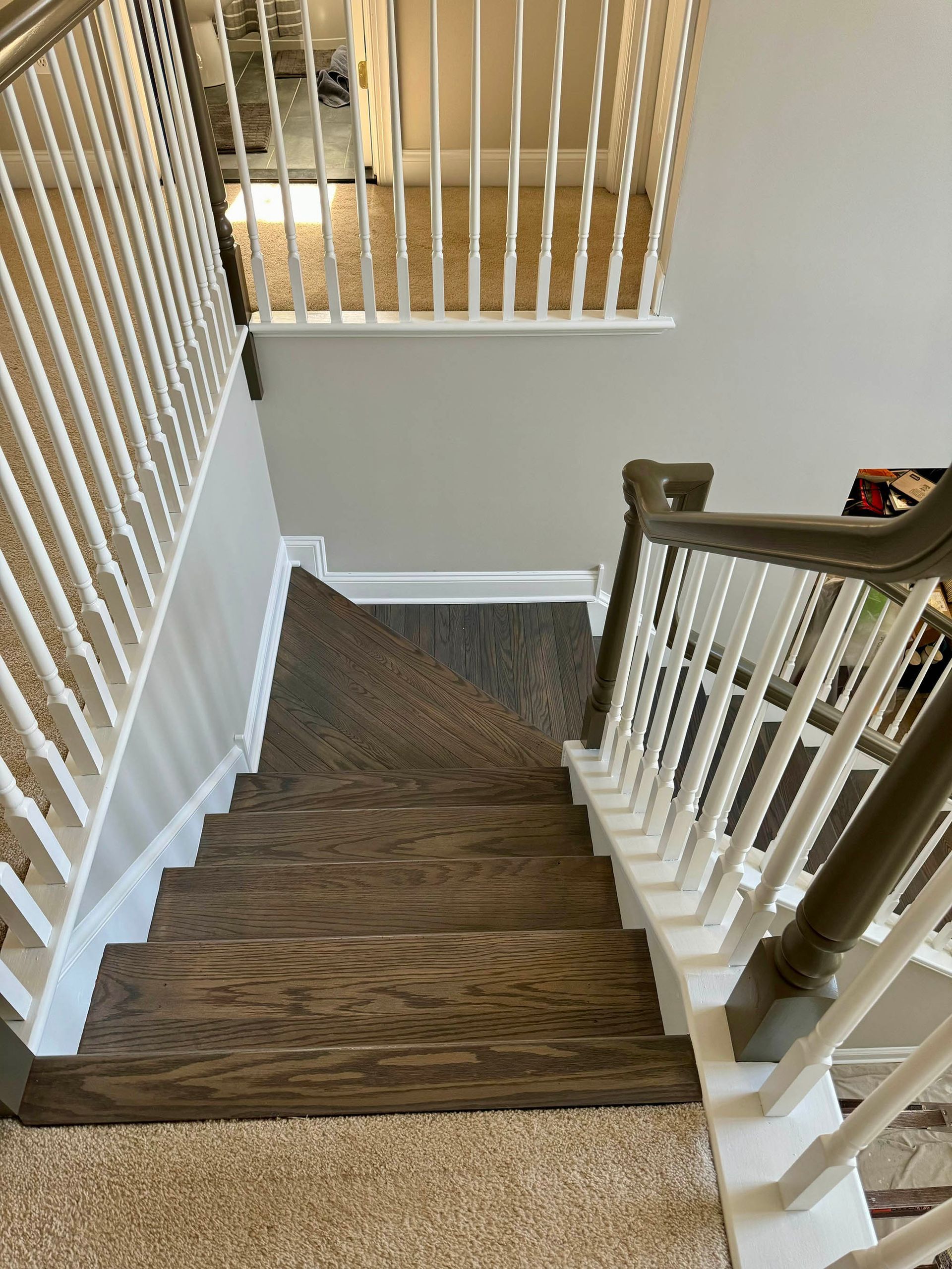 Staircase with brown wooden steps, white railings, and tan carpet.