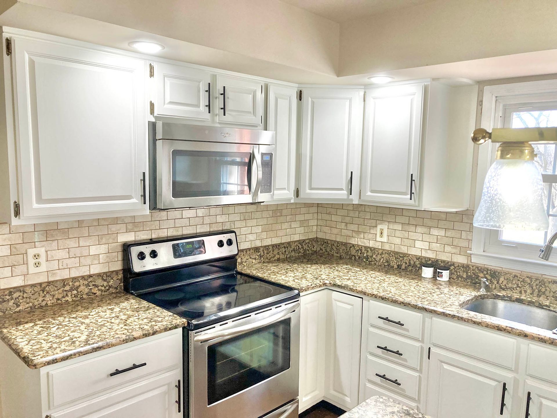 White kitchen with granite countertops, stainless steel appliances, and tile backsplash.