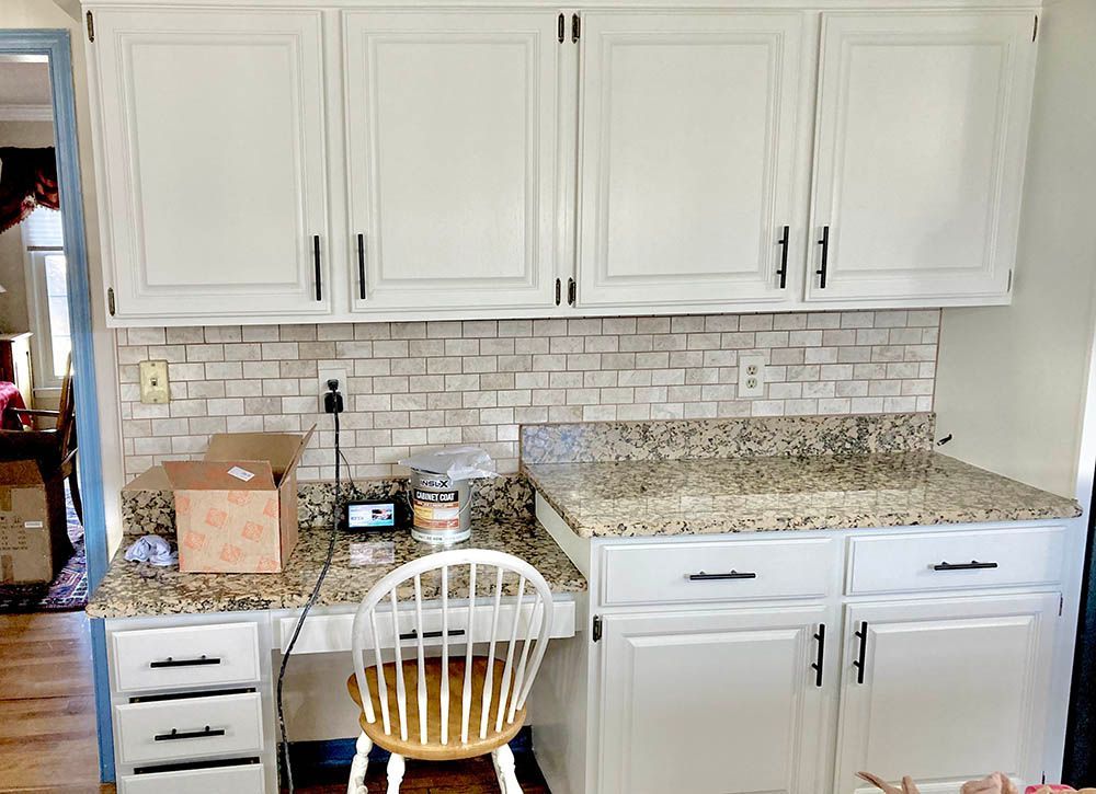 Kitchen with white cabinets, speckled countertop, and a desk area with a chair.