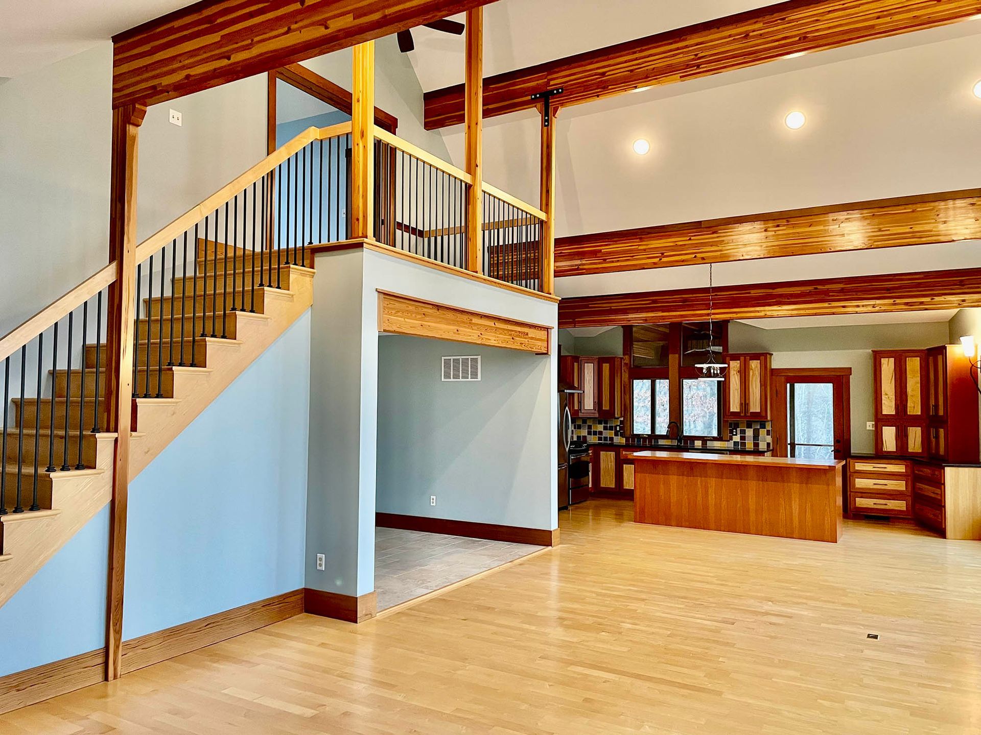 Spacious interior with staircase, kitchen, wood beams, and light blue walls.