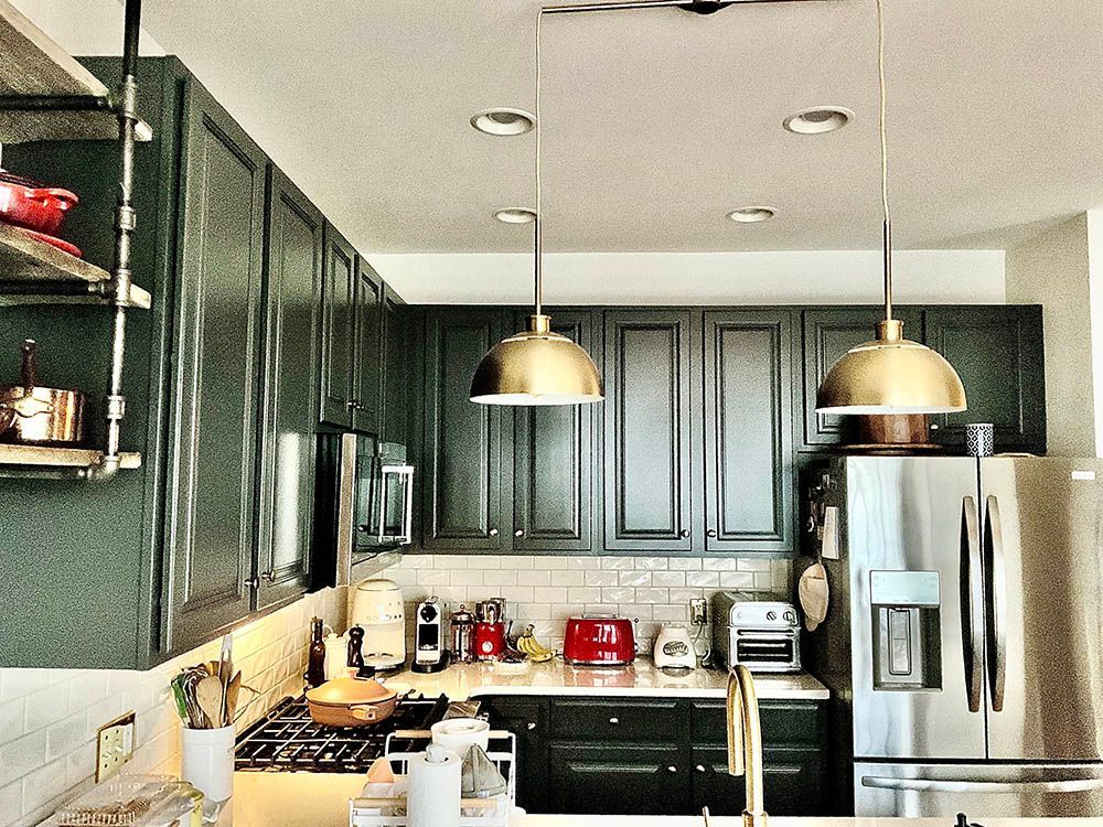 Kitchen with dark green cabinets, stainless steel refrigerator, and gold pendant lights.