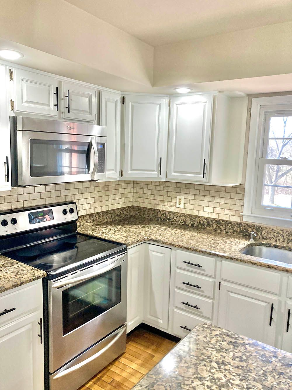 White kitchen with stainless steel appliances, granite countertops, and a window.