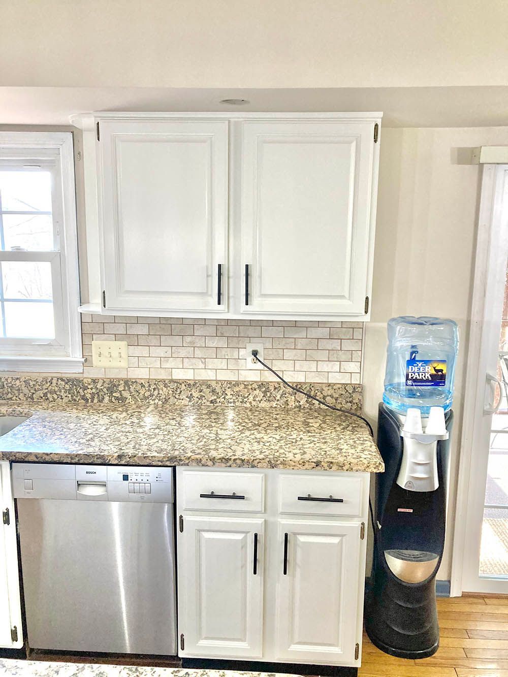 White kitchen cabinets and granite countertop with a dishwasher and water cooler.