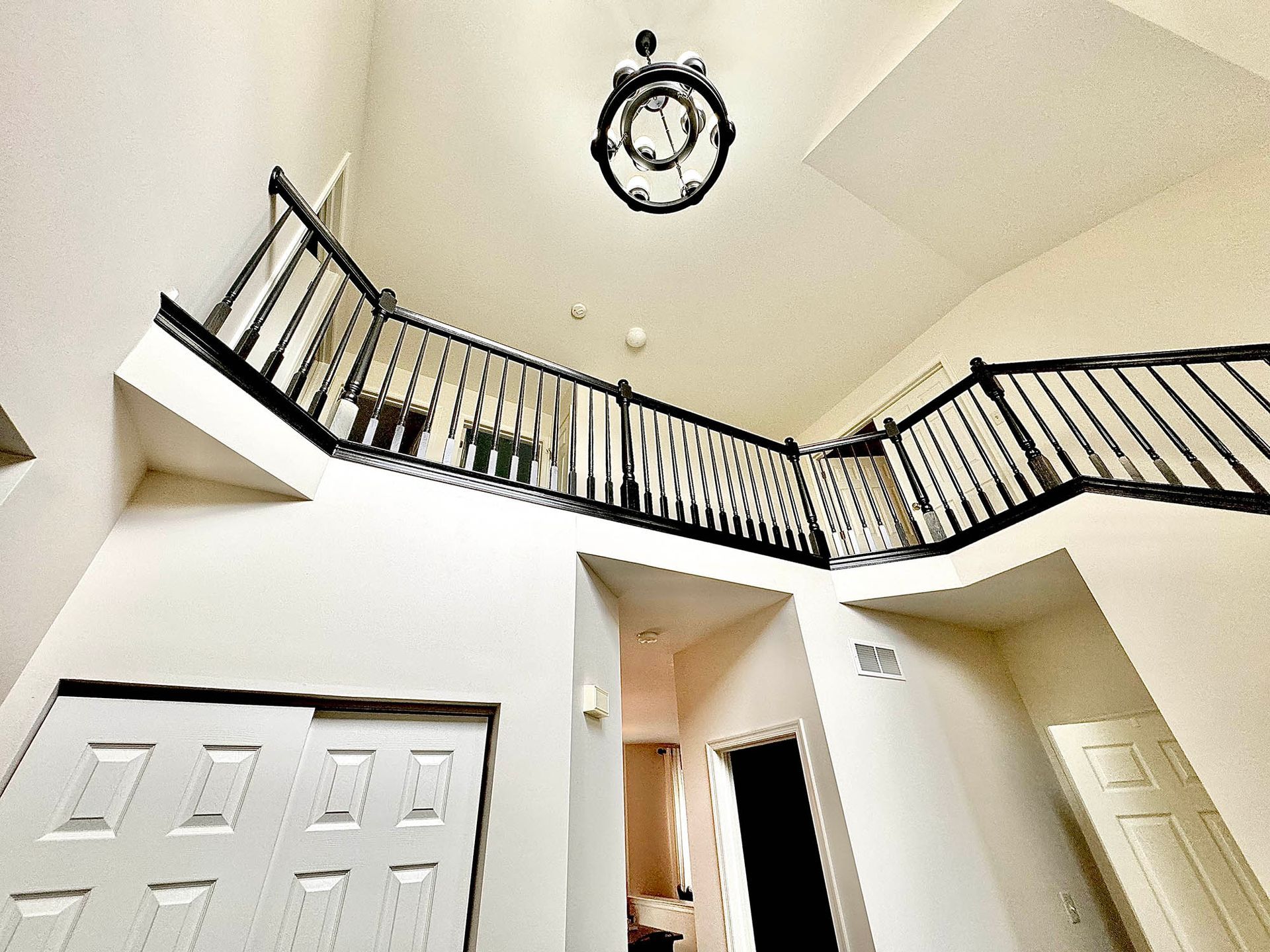 Interior view of a two-story foyer with a staircase, black railings, and a chandelier. White walls and doors.