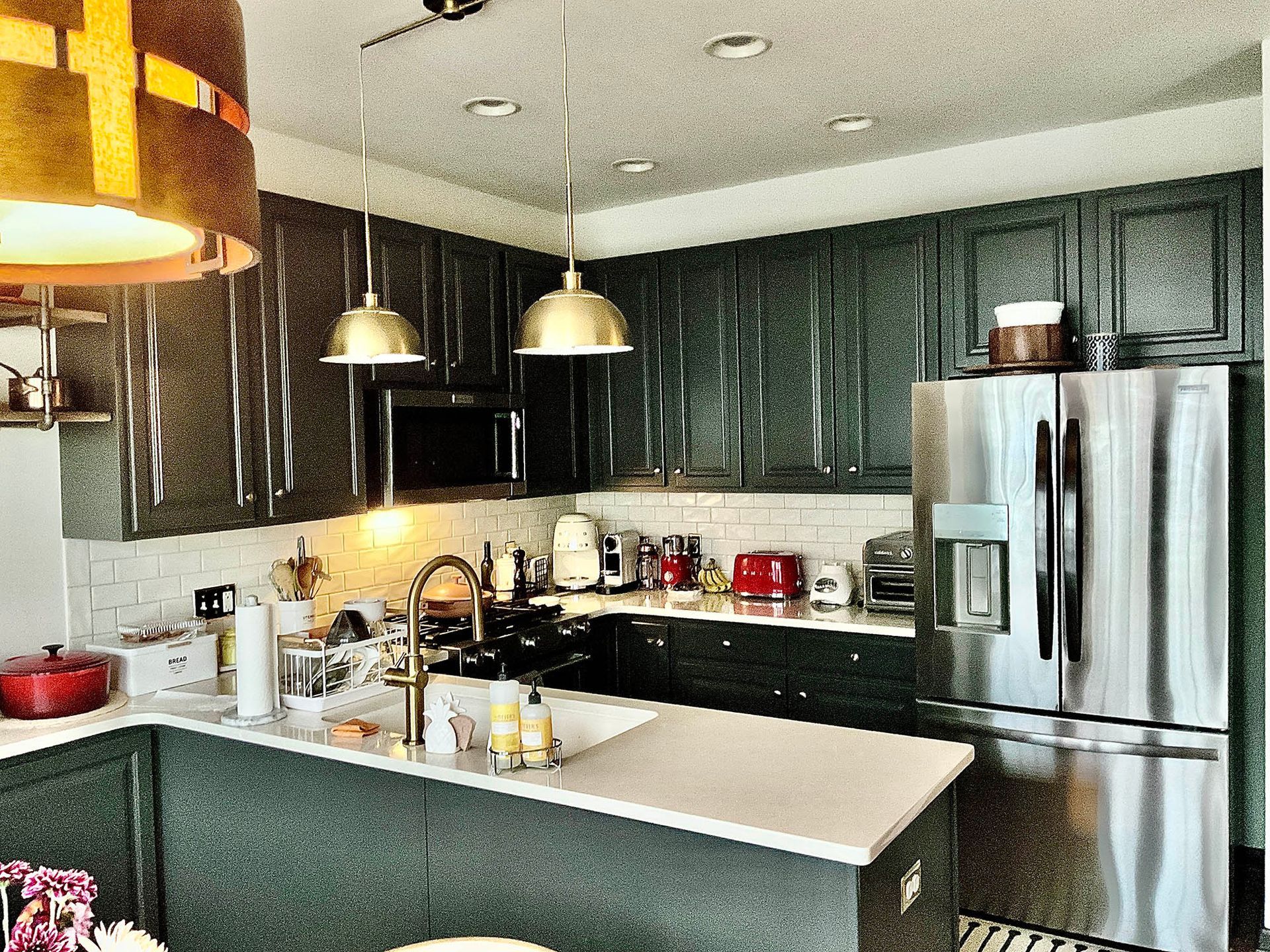 Kitchen with dark green cabinets, stainless steel fridge, white countertops, and pendant lights.